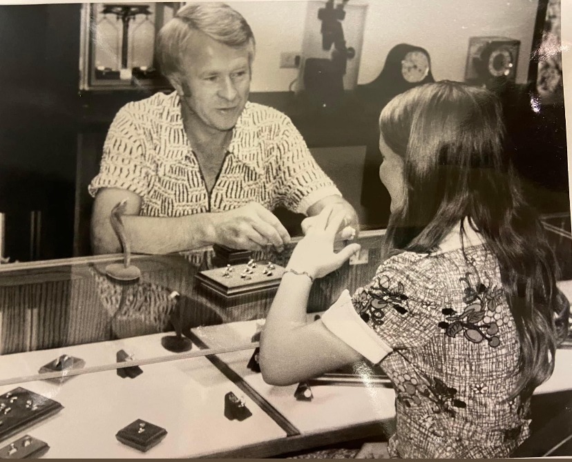 A jeweler assists a young woman in a shop, showcasing rings on a display table