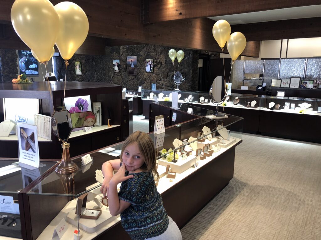 A young girl poses playfully in a jewelry store, surrounded by displays of necklaces and rings